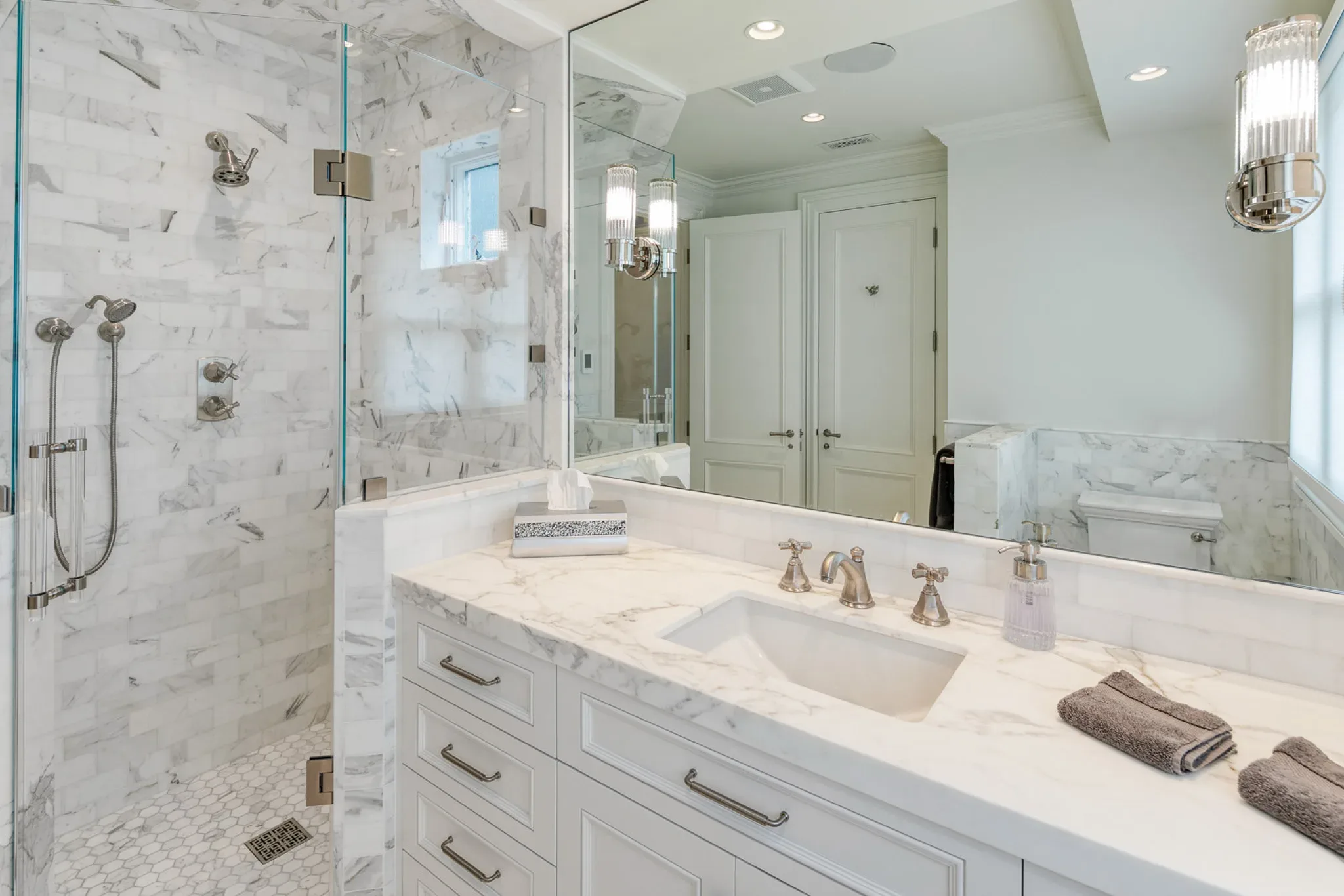 A white bathroom with marble counter tops and a walk in shower.