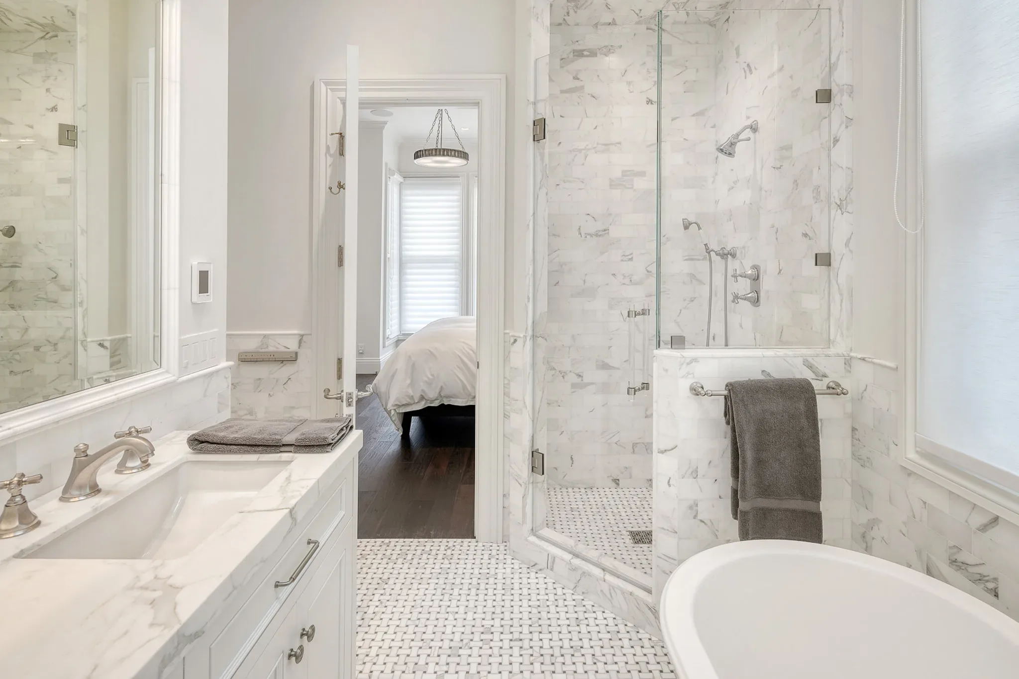 A white bathroom with marble floors and a glass shower.